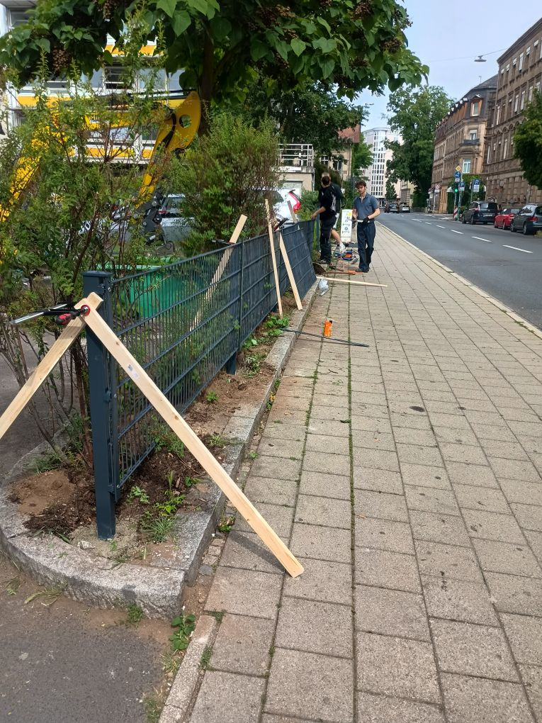 Schüler arbeiten an Zaun. Bagger ist zu sehen